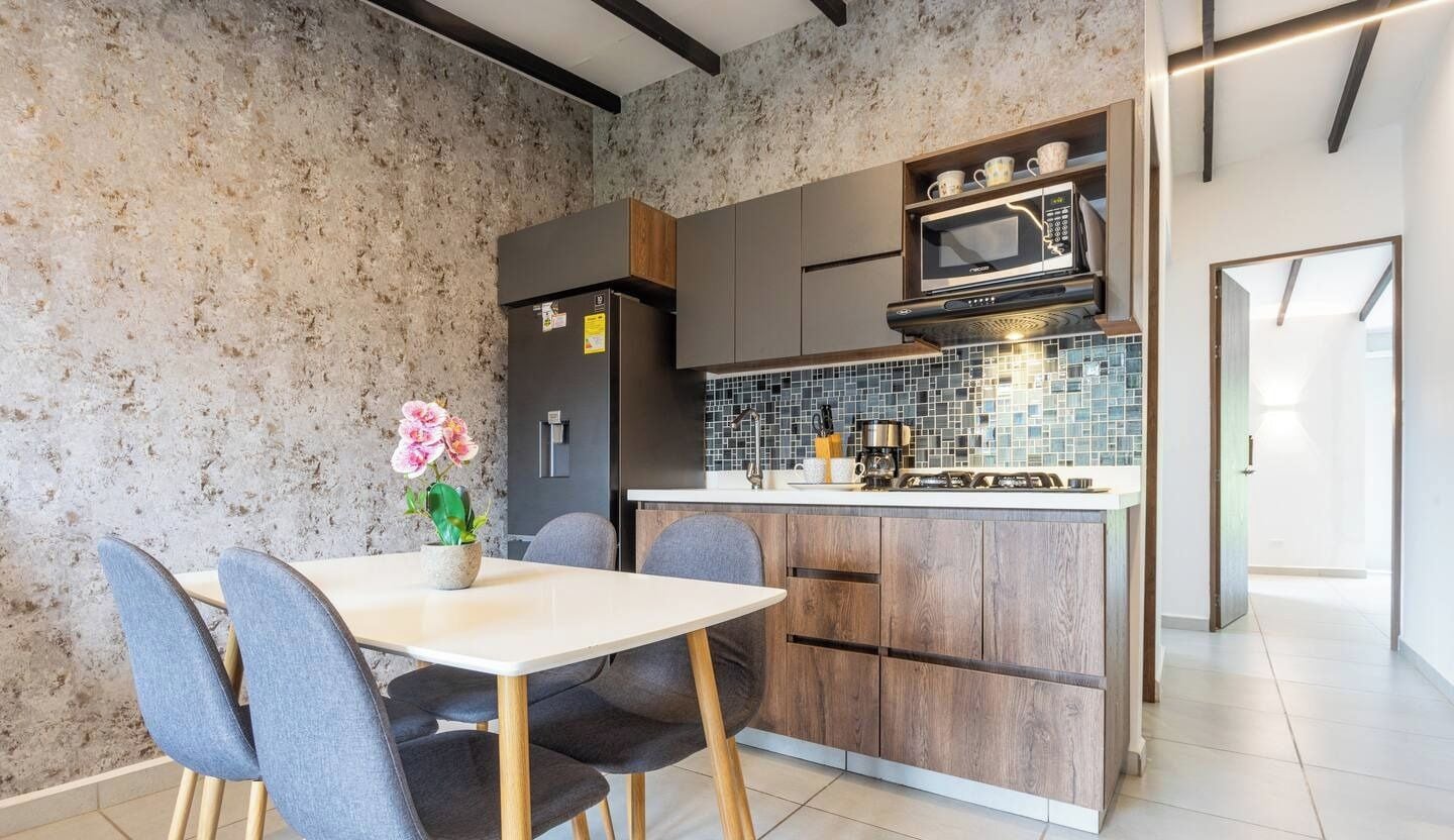 A modern kitchen with a central island, grey chairs, and a small potted plant.