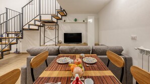 A modern living room with a dining table set for two, a sofa, a TV, and a staircase. - Loft 'Kiccifù Home Palermo' with Wi-Fi and Air Conditioning (Palermo)