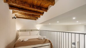 A bedroom with a bed, wooden ceiling beams, a balcony with a railing, and a bathroom visible through an open door. - Loft 'Kiccifù Home Palermo' with Wi-Fi and Air Conditioning (Palermo)