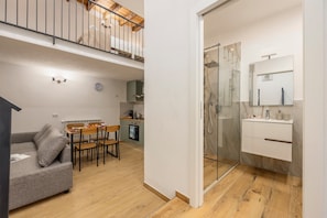 A modern apartment with a dining area, kitchenette, and a glass shower enclosure.