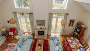 Un salon spacieux doté d’une cheminée, de deux grandes fenêtres, d’un coin repas et d’un espace salon confortable.