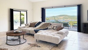 Ein modernes Wohnzimmer mit einer Couch, einem Couchtisch und Blick auf eine Küstenlandschaft durch große Fenster.
