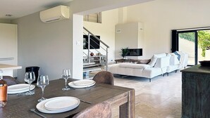 Ein moderner Essbereich mit einem Holztisch, gedeckt für vier Personen, einem Sofa im Hintergrund und einer Treppe, die zu einer oberen Ebene führt.