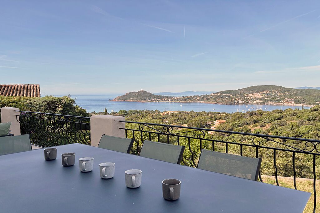 A terrace with a table and chairs overlooking a coastal landscape with hills and a body of water.