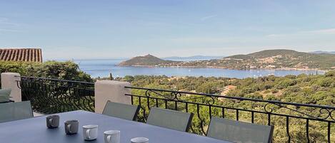 A terrace with a table and chairs overlooking a coastal landscape with hills and a body of water.