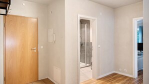 A hallway with a wooden door, a glass shower door, and a tiled floor.