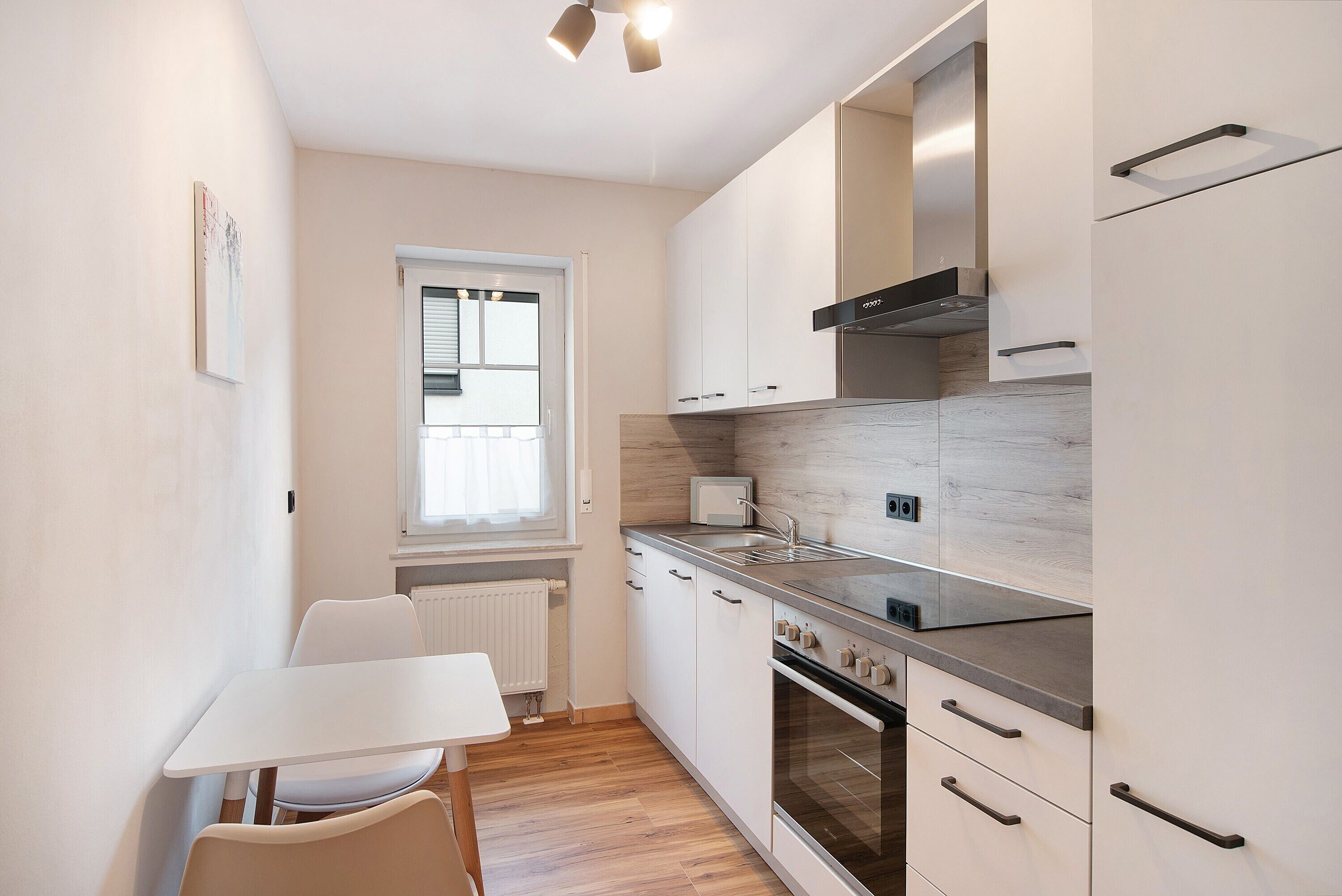 A modern kitchen with white cabinets, a built-in oven, and a window with blinds.