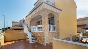 A residential property with a stone facade, a staircase with white balustrades, and a tiled patio area.