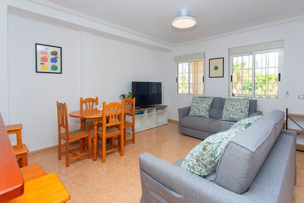 A living room with a sofa, a TV, a dining table with chairs, and a window with a view.