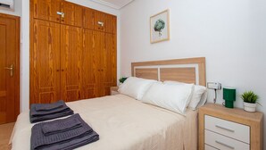A bedroom with a bed, a wooden wardrobe, a bedside table with a lamp, and a wall-mounted plant.