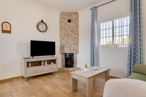 A living room with a TV, fireplace, wooden furniture, and a window with curtains.