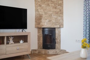 Un salon avec un téléviseur, une cheminée en pierre, un meuble en bois et un vase rempli de fleurs.