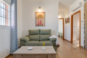 Un salon avec un canapé vert, une table basse en bois, une œuvre d’art accrochée au mur et une porte donnant sur une autre pièce.