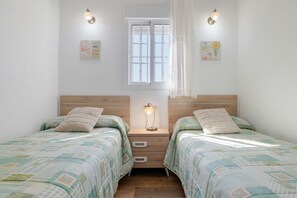 A bedroom with two beds, a nightstand with a lamp, a window with curtains, and wall decorations.