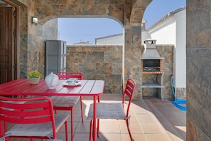 An outdoor patio with a red table and chairs, a stone wall, and a barbecue grill.