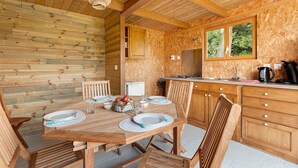 Un intérieur en bois comprenant une table à manger pour quatre personnes, un coin cuisine et une fenêtre donnant sur un paysage verdoyant.