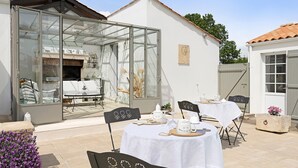 Une terrasse dotée d’une véranda en verre, d’un espace salon extérieur et d’une table blanche dressée pour le repas.