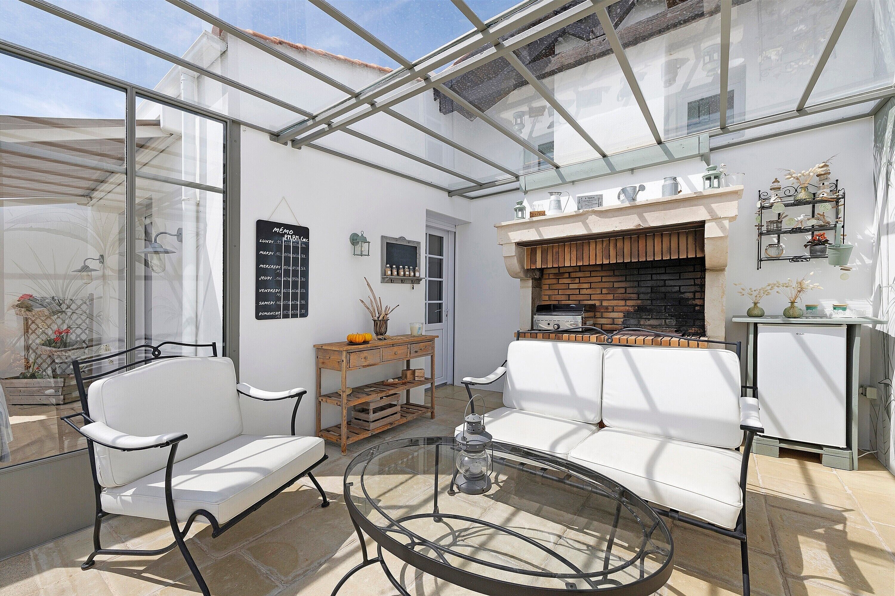 A conservatory with a glass ceiling, white furniture, a brick fireplace, and a small table with a lantern.