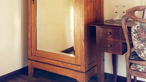 Un meuble en bois avec un miroir, un petit bureau avec deux verres à vin et une chaise à motifs floraux.