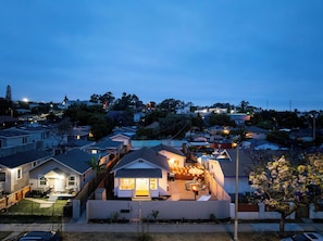 Um bairro residencial com casas, um quintal com churrasqueira e uma árvore florida.