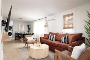 Uma sala de estar moderna com um sofá marrom, mesa de centro redonda e um espaço de jantar com mesa e cadeiras.