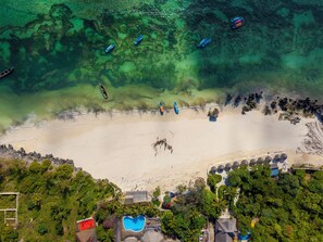 An aerial view of a beach with clear water, boats, and a pool area with umbrellas. - The Swahili Plaza (Matemwe)