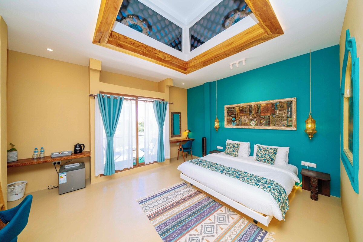Een slaapkamer met een bed, bureau, stoel, plafondventilator en een raam met gordijnen.