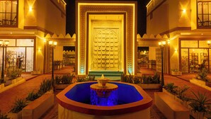 A courtyard with a central fountain, surrounded by buildings with ornate facades and warm lighting. - The Swahili Plaza (Matemwe)