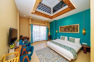 Habitación de hotel con cama, escritorio con silla, televisor y balcón con vistas.