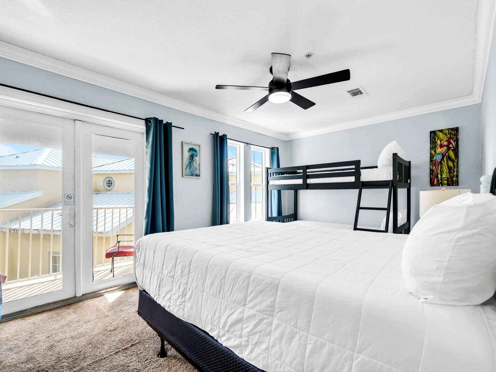Een slaapkamer met een stapelbed, een plafondventilator, een raam met gordijnen en een balkon met een balustrade.