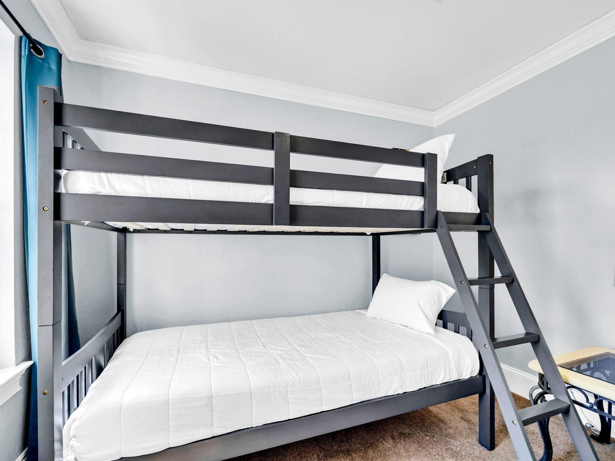 Una litera con escalera, ropa de cama blanca y una mesita de noche a un lado.
