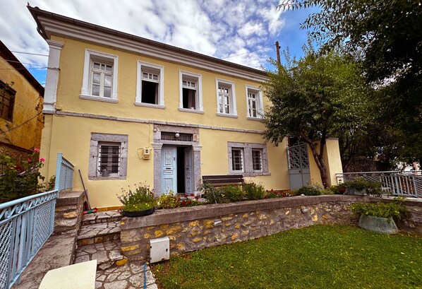 A two-story building with a stone staircase leading to the entrance, a small garden with flowers, and a bench outside. - The Dream Villa Kastoria (Kastoria)