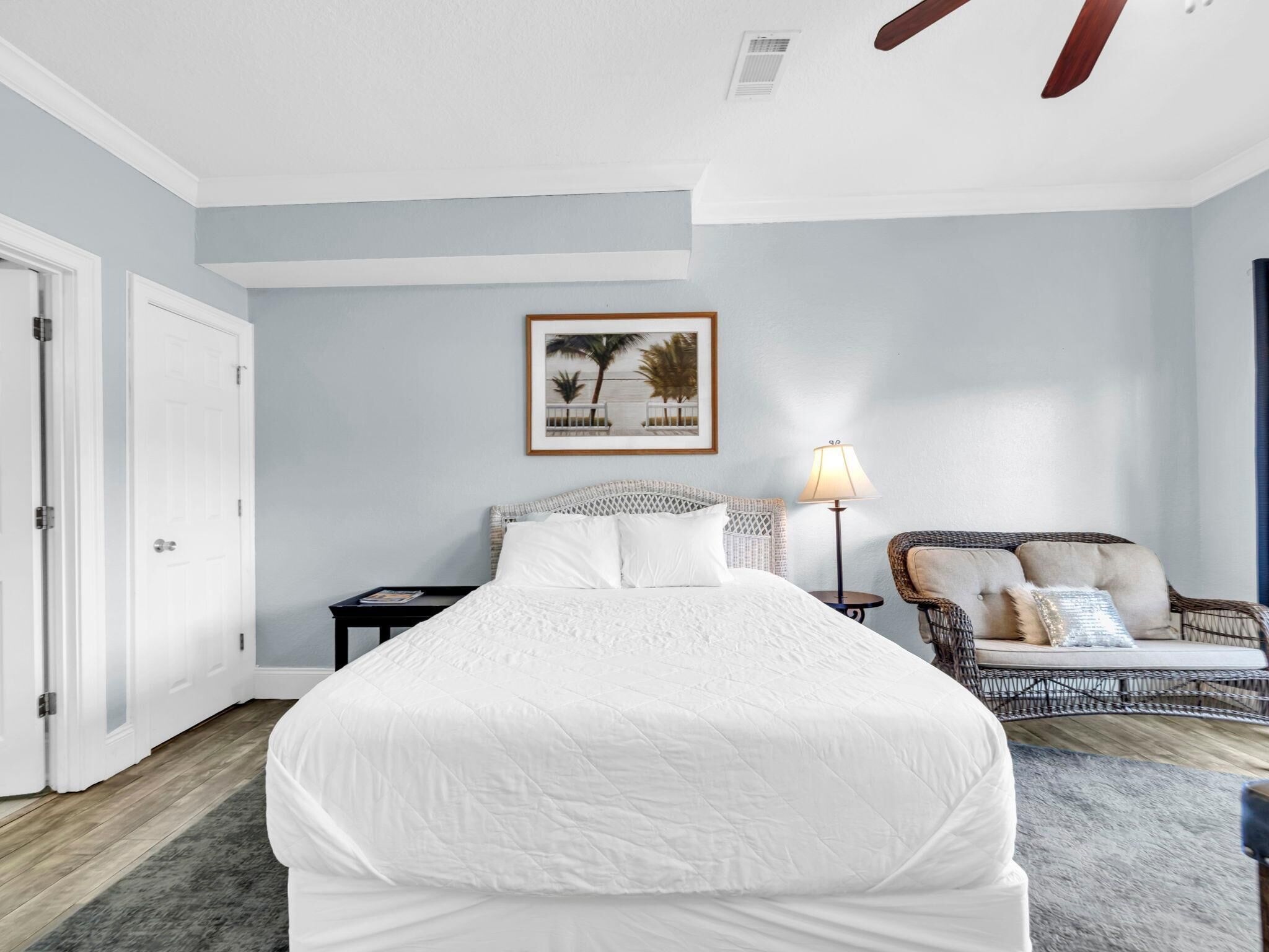 A bedroom with a large bed, a chair, a nightstand, a lamp, and a framed picture on the wall.