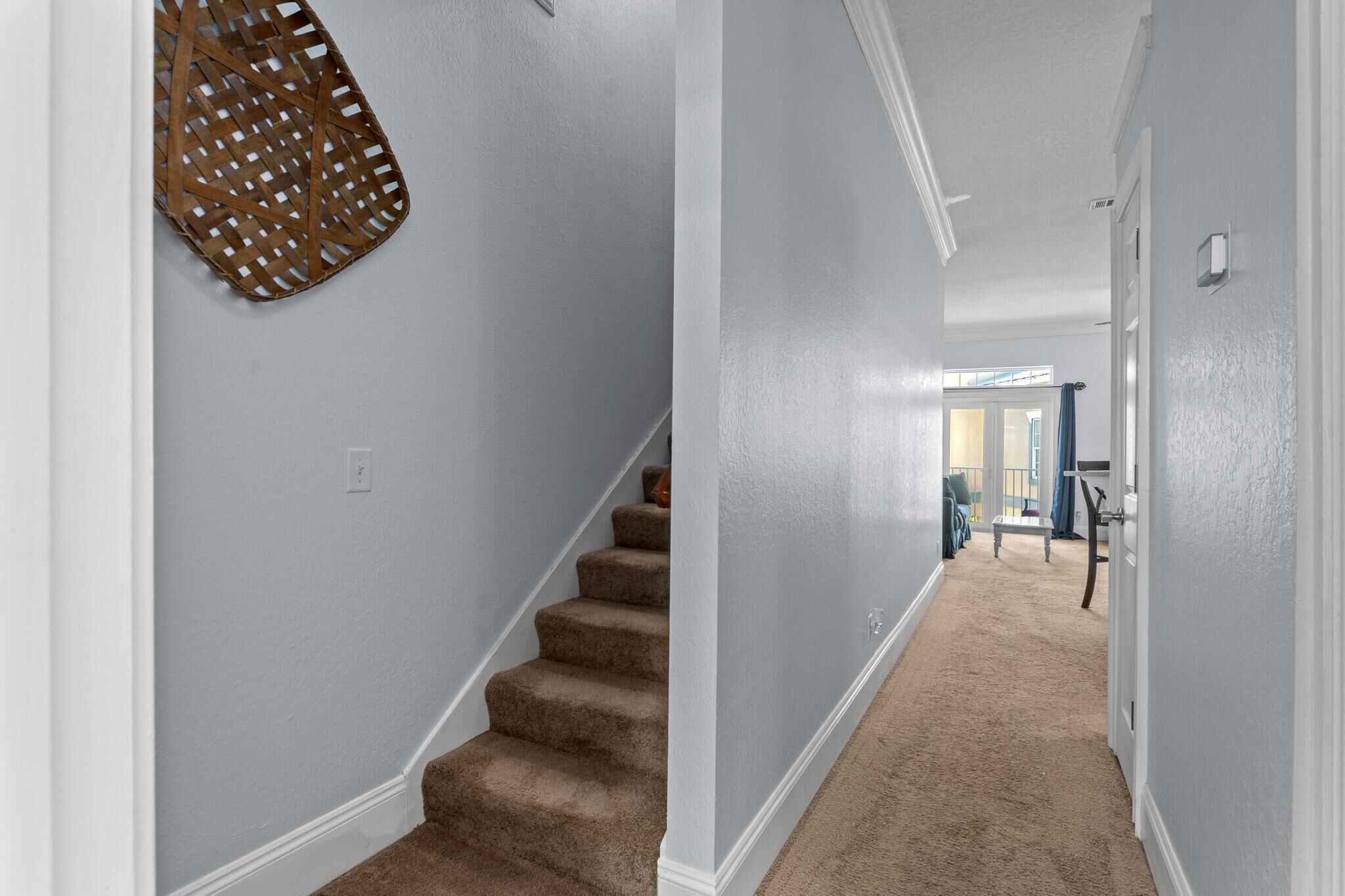 A hallway with a carpeted staircase, a light blue wall, and a hanging basket.