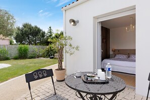 Une terrasse avec une table ronde, un pot de fleurs et un lit visible à travers une porte ouverte.