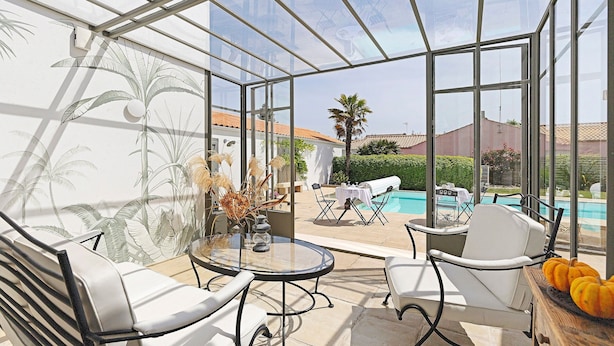 Un invernadero con paredes de vidrio, una piscina, muebles blancos y un mural tropical.