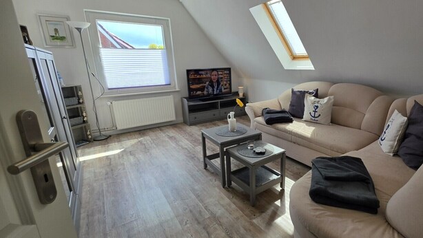 A modern living room with a sofa, a coffee table, a television, and a window with blinds.