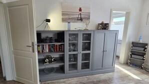 A room with a grey cabinet, a bed with floral bedding, a desk with a lamp, and a window with blinds.