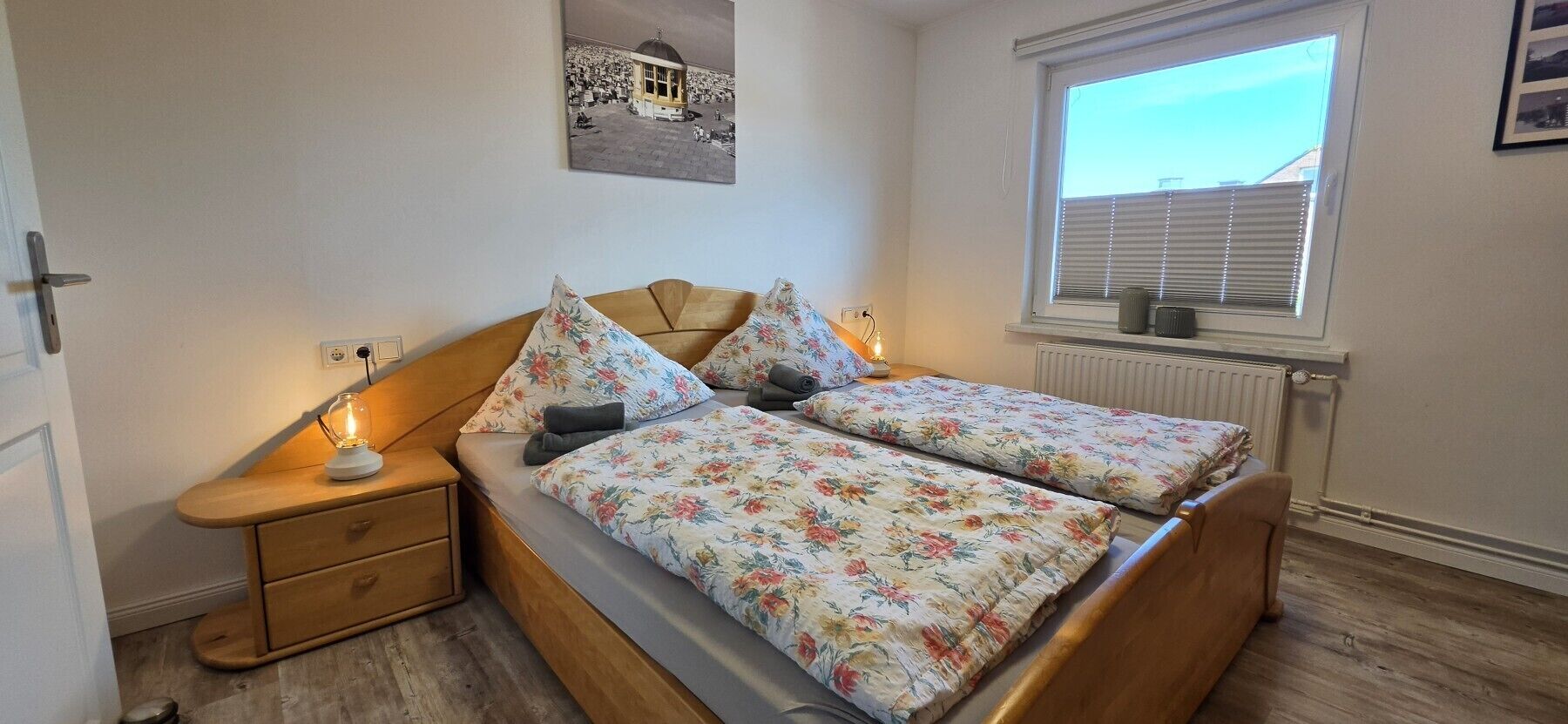 Een slaapkamer met een bed, nachtkastjes, een radiator en een raam met jaloezieën.