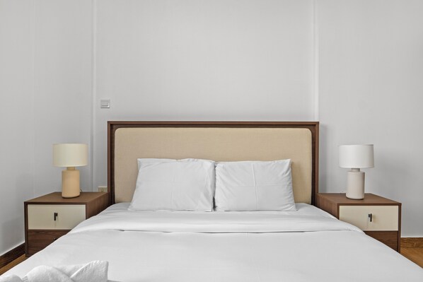 A neatly made bed with white linens, two bedside tables with lamps, and a wooden headboard.