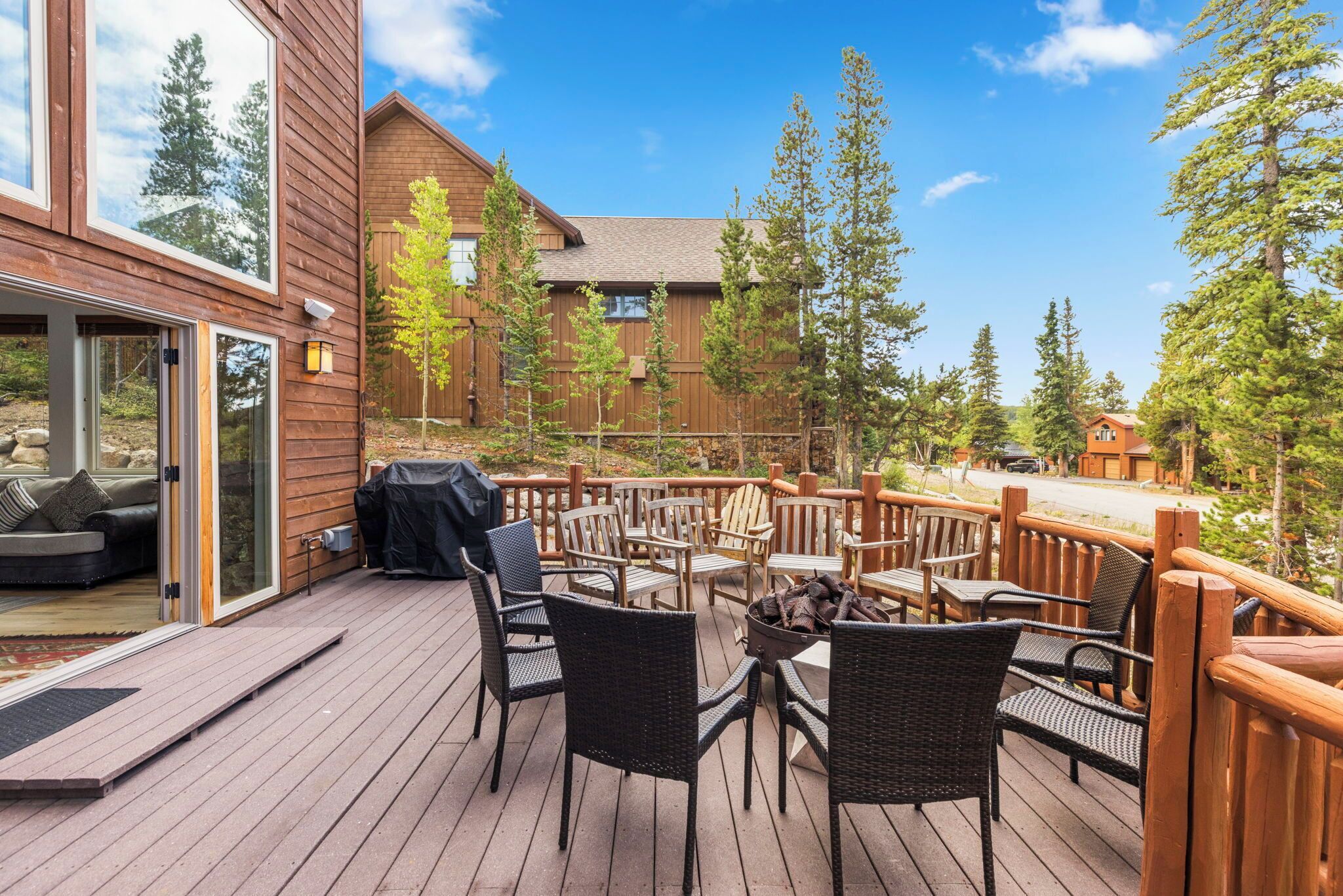 A wooden deck with outdoor furniture, a fire pit, and a view of a building with large windows and a deck railing.
