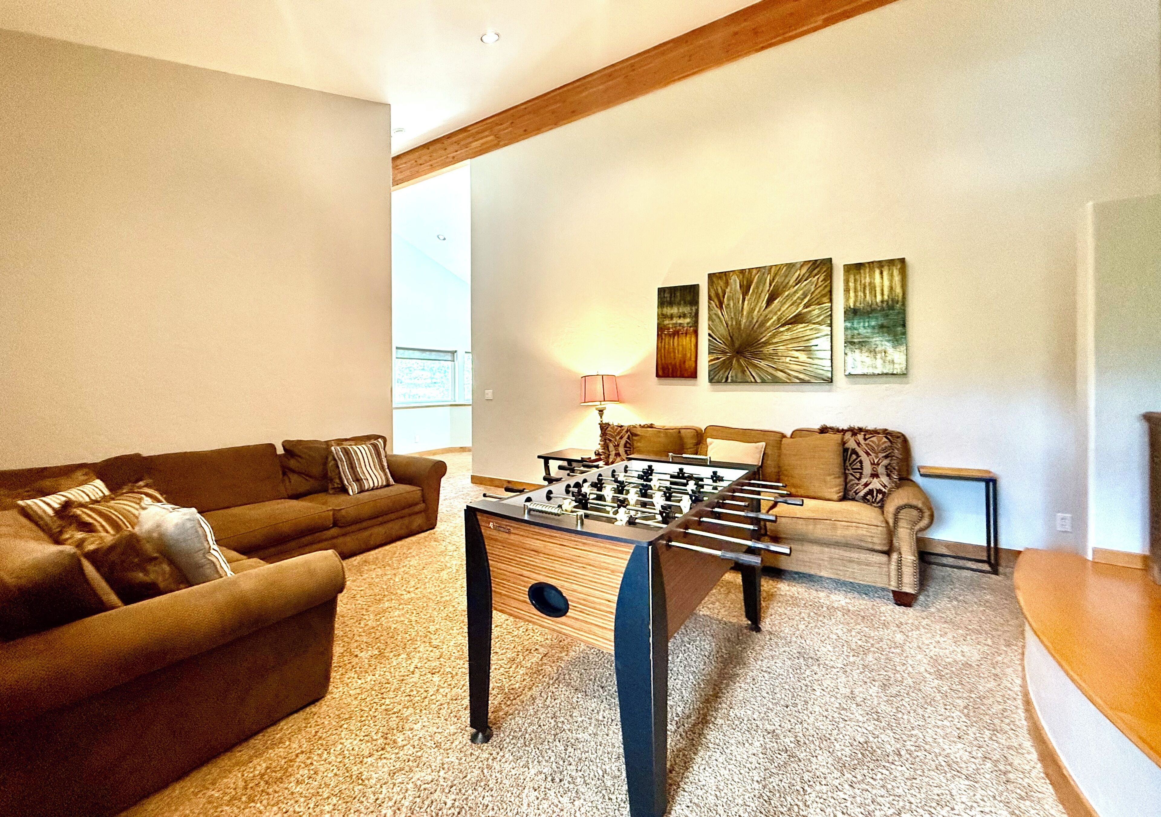 A living room with a foosball table, sofas, and artwork on the wall.