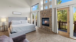 A bedroom with a stone fireplace, a large bed, and a view of the outdoors through a sliding glass door. - Fox Den at Emmett Lode (Breckenridge)