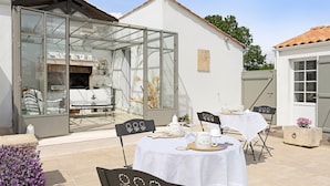 Un patio con cerramiento de vidrio, mobiliario exterior y una mesa blanca dispuesta para comer.