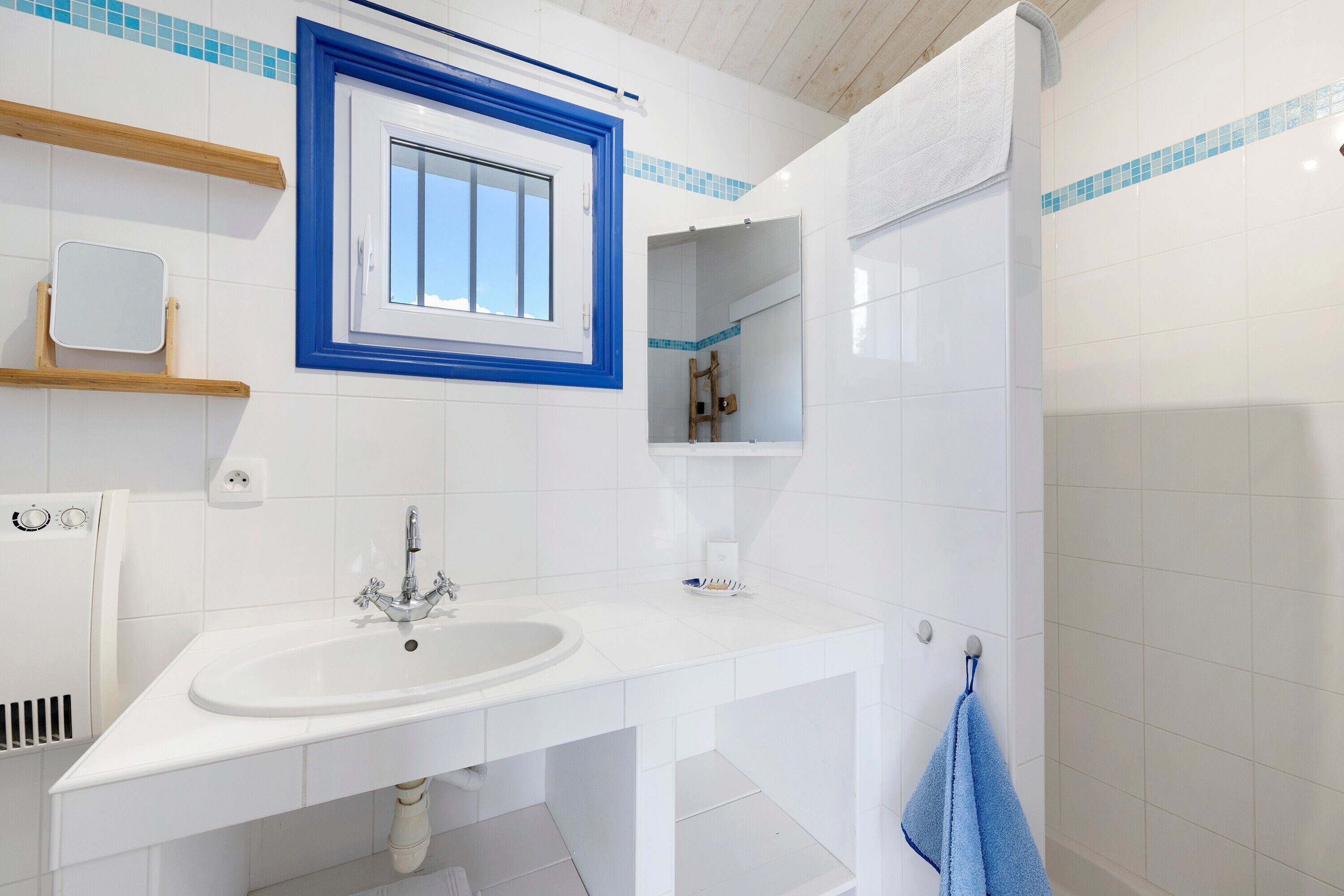 Een badkamer met een witte wastafel, een spiegel, een handdoekhouder en een douche.