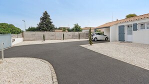 Una zona residencial con un camino pavimentado, un coche blanco estacionado y un edificio con tejado de tejas.