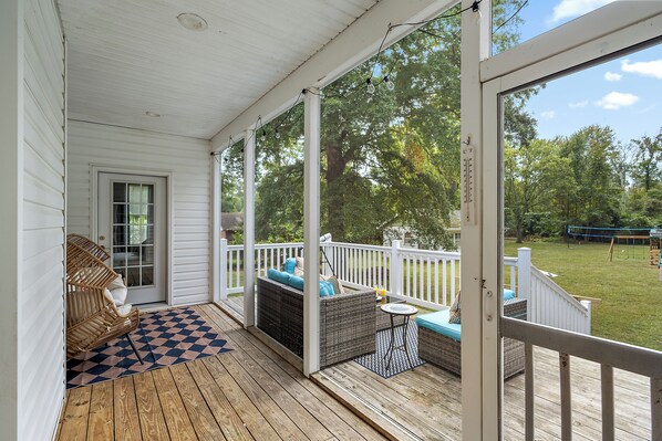 A covered porch with wicker furniture, a checkered floor, and a view of a grassy yard.