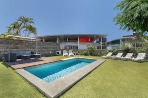 Un espace piscine moderne avec une piscine rectangulaire, des chaises longues et un mur en pierre.