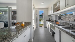 A modern kitchen with granite countertops, white cabinets, and a view to an outdoor patio. - Vacation Villa 'Playa Del Duque' with Private Terrace, Wi-Fi and Air Conditioning (Adeje)