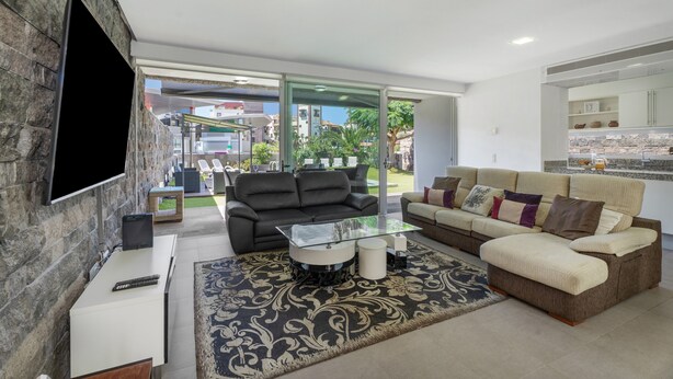 A modern living room with a glass coffee table, two sofas, a TV, and a stone accent wall. - Vacation Villa 'Playa Del Duque' with Private Terrace, Wi-Fi and Air Conditioning (Adeje)
